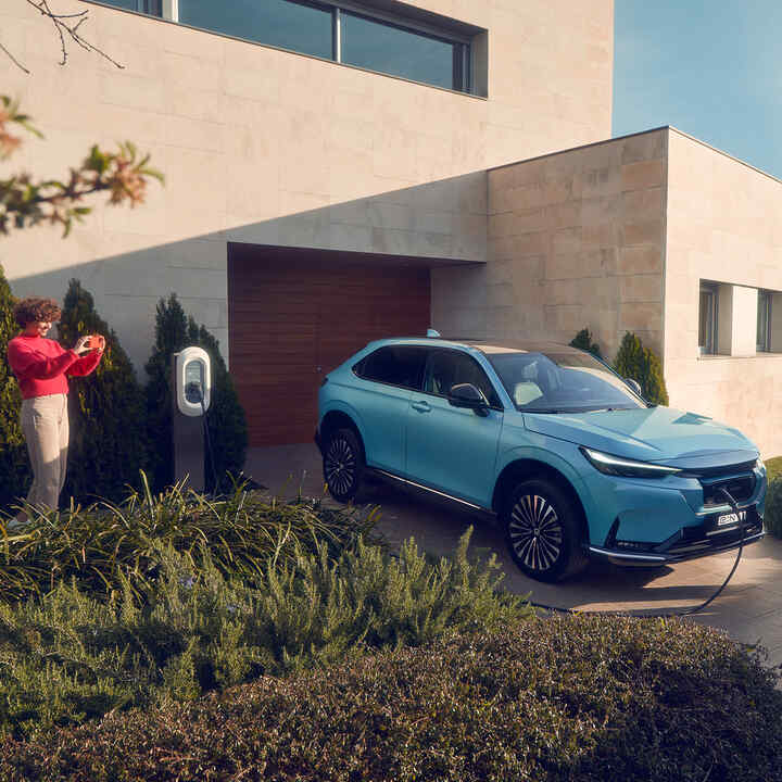 Family playing on driveway next to Honda e:Ny1 charging in the driveway.