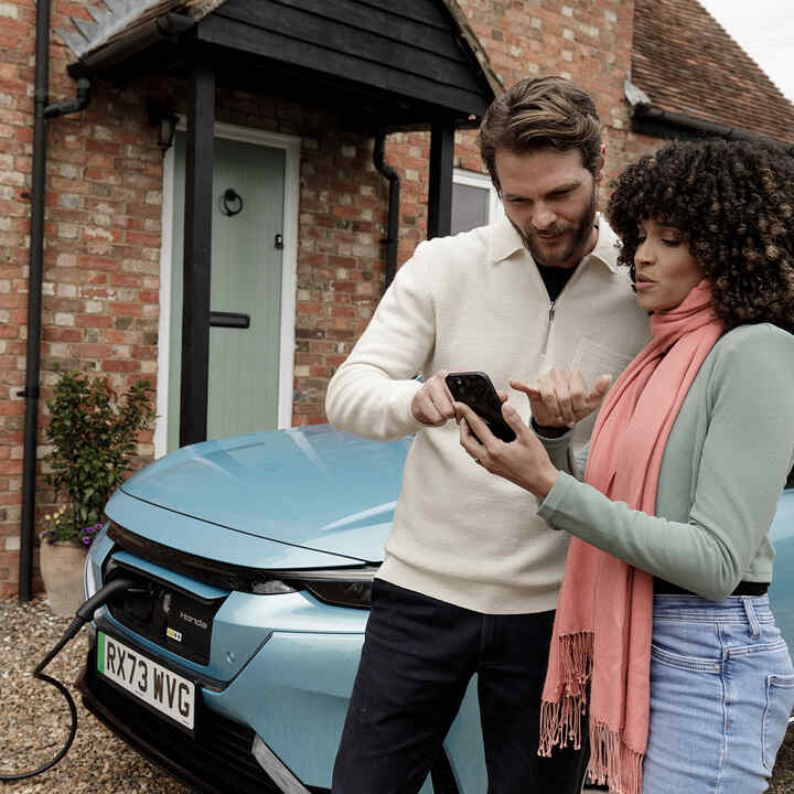 Model holding a phone with a close up of the Honda E charging system.