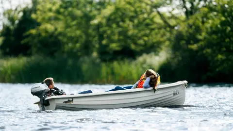 Two people laying down in a boat on the water with a Honda engine.