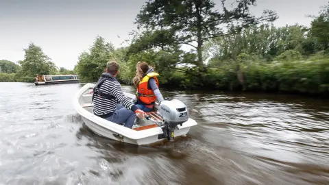 Two people in a boat using the BF2.3 engine, next to a canal boat.