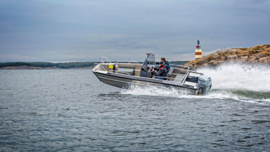 Model steering a boat in a sea location with the BF80-100 engine.